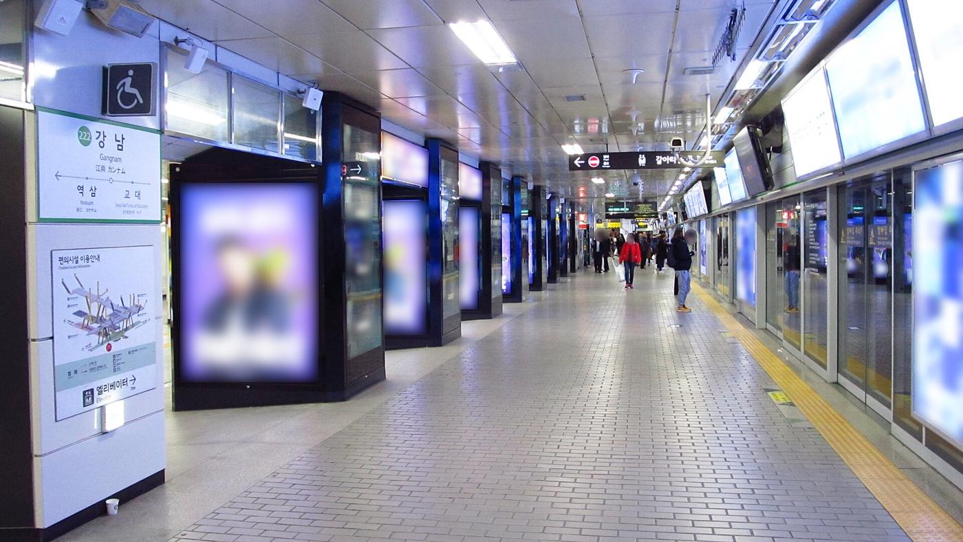 The Line 2 platform at Gangnam Station: green 222 Gangnam sign, a row of lit advertising panels along a tiled platform, and screen doors on the right.
