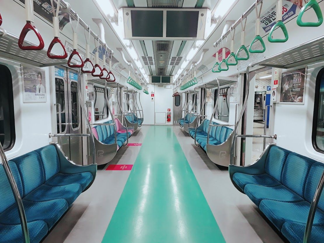 The inside of an empty Seoul Metro Line 2 car: blue bench seats, green and red hand straps, a green floor stripe.