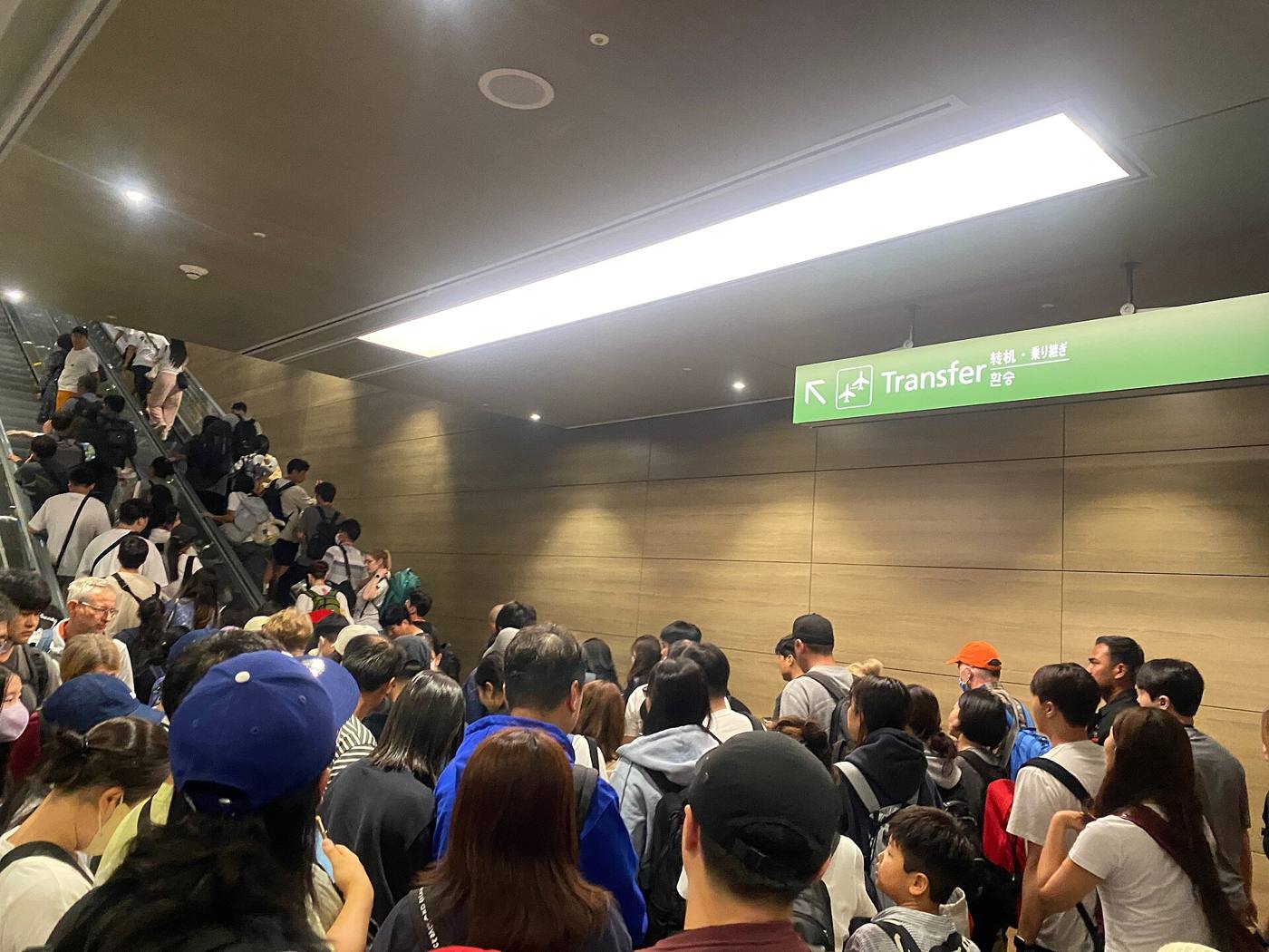 A dense crowd of arriving passengers filling a corridor below a green Transfer sign at Incheon International Airport, some on an escalator.