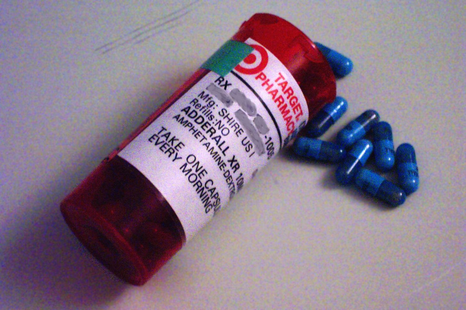 A red pharmacy prescription bottle labelled Adderall XR lying on its side with blue capsules spilling out.