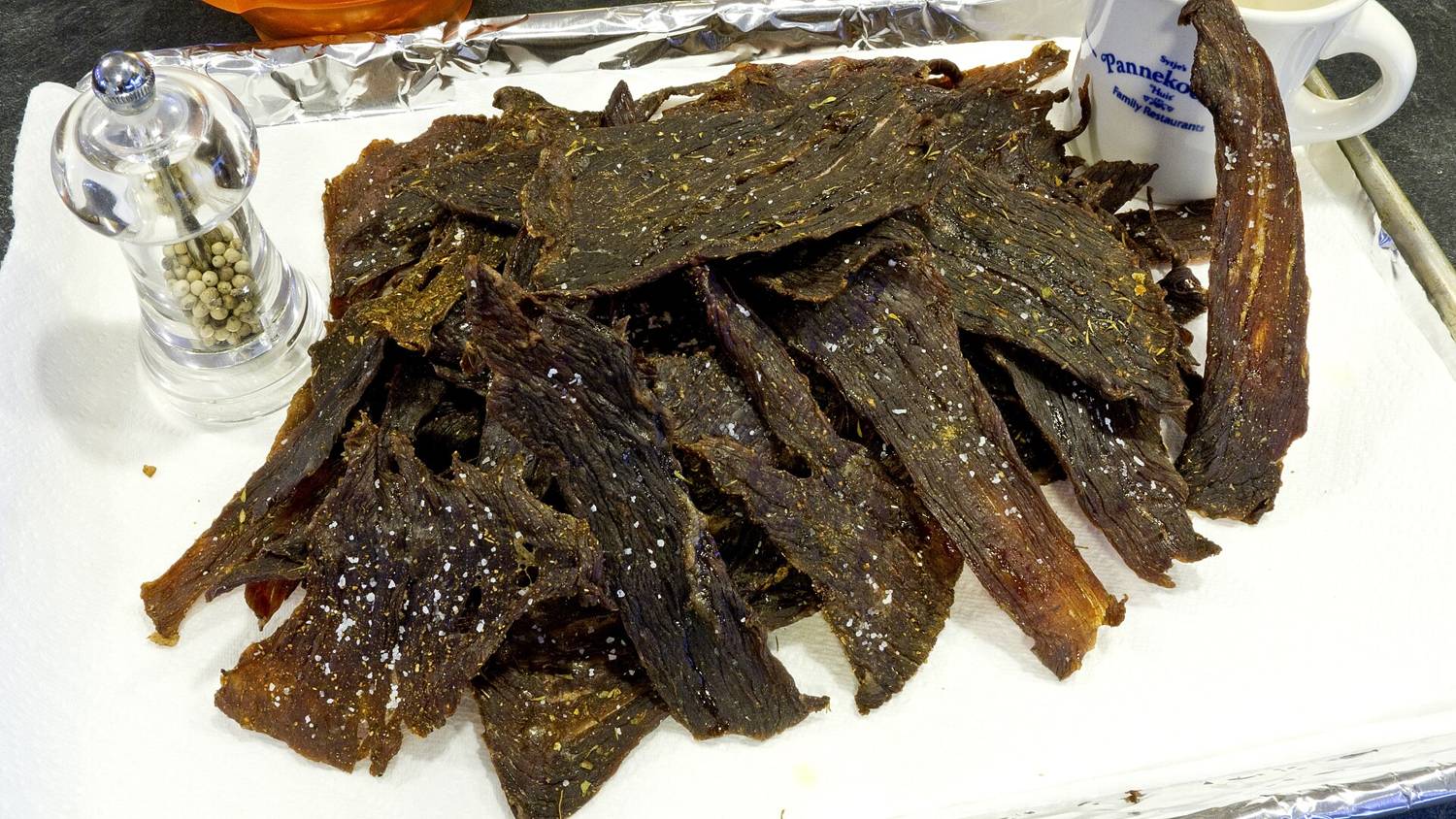 A pile of dark, dried beef jerky strips on a paper-lined tray.