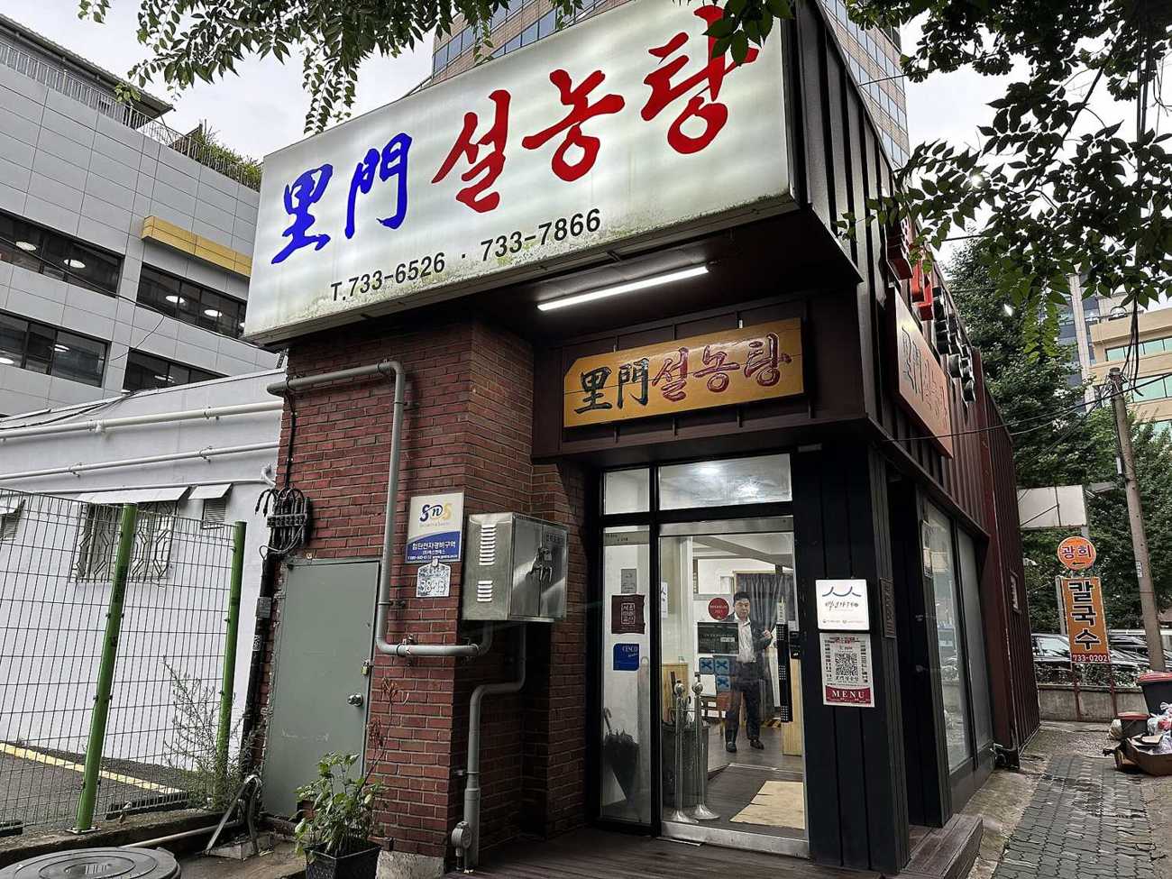 The corner entrance of Imun Seolnongtang in Jongno: a brick building with the large 里門설농탕 signboard above, a wooden sign over the glass door, and the Seoul Future Heritage and 백년가게 plaques beside it.