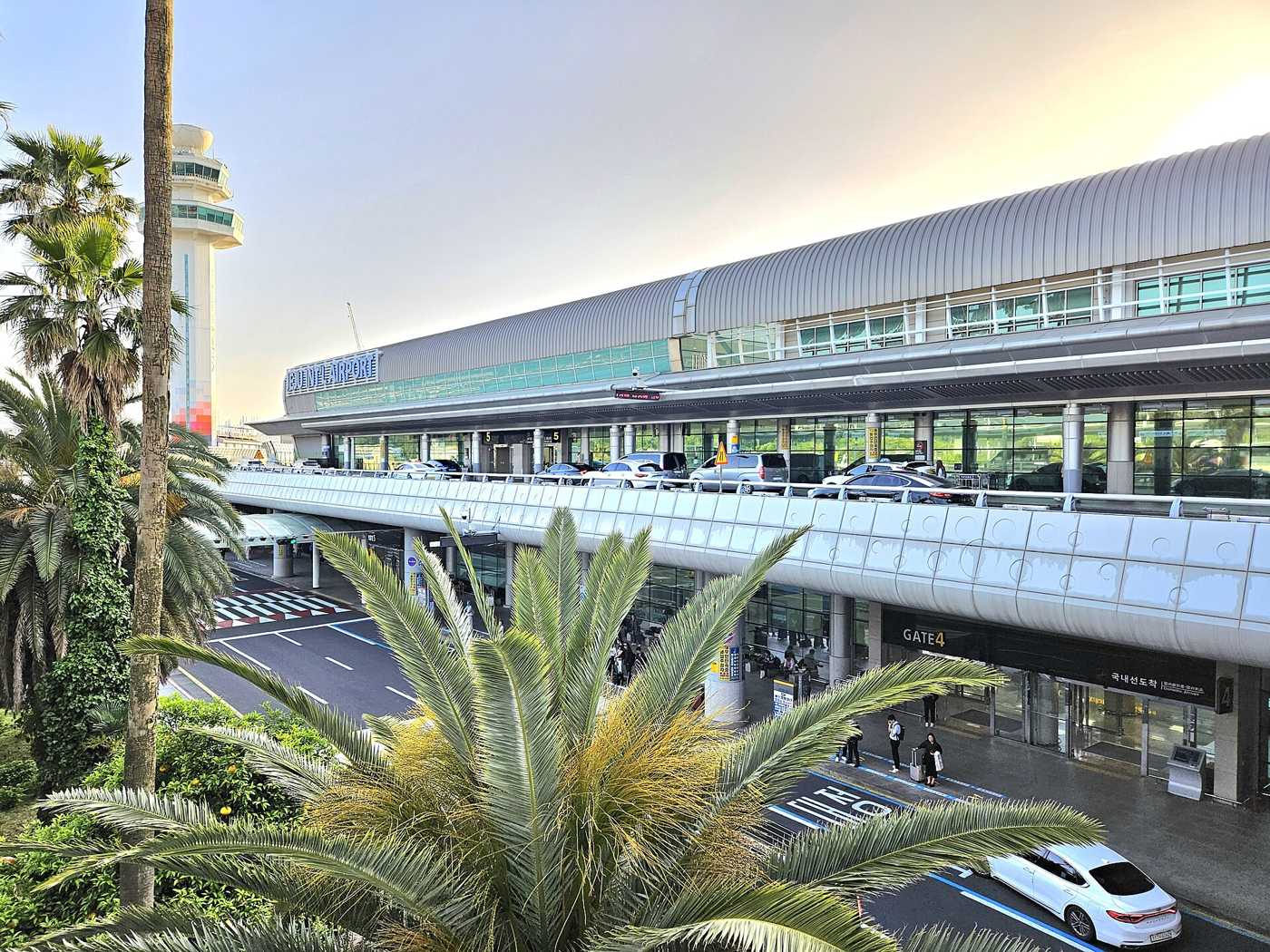 Jeju International Airport's terminal building at dusk, with the domestic arrivals entrance and taxis in front.