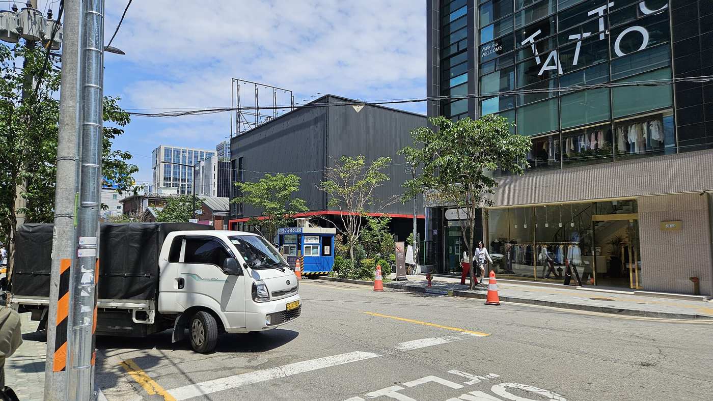 A Seongsu-dong street in May 2026: a black metal-clad warehouse building, a parked truck and a glass-fronted clothing store.