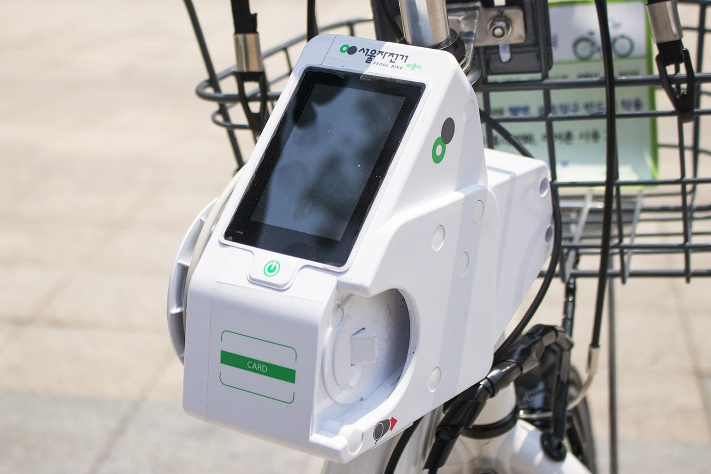 The terminal mounted on an older Ttareungi bike: a white terminal with a small screen, a power button and a card pad, mounted in front of the basket.