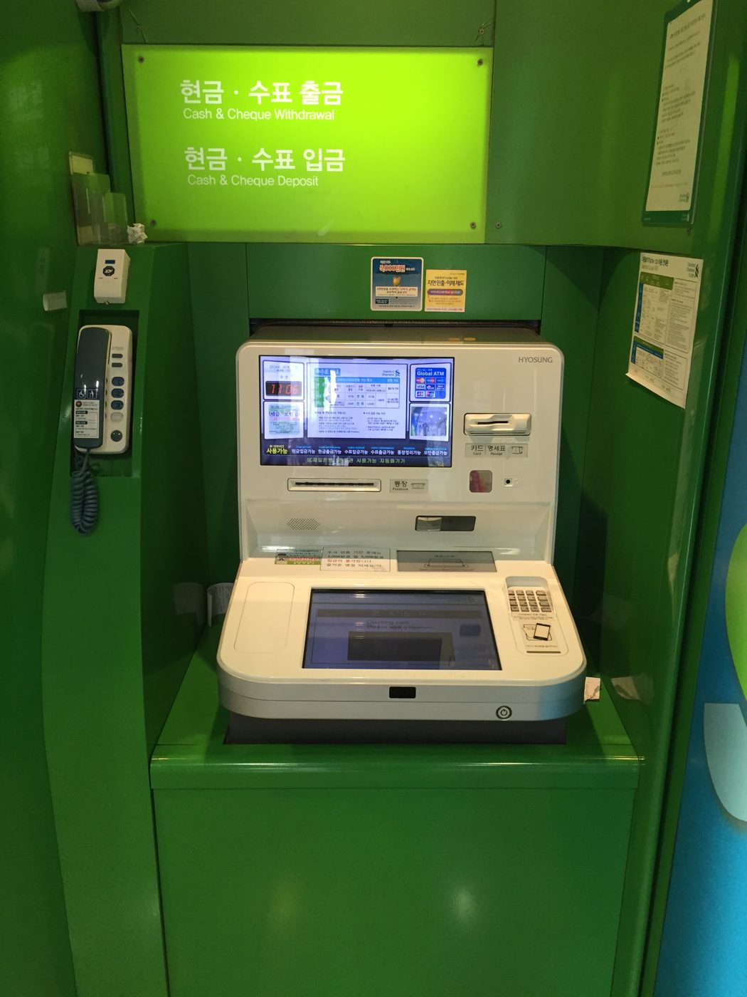 A green Standard Chartered cash machine in Seoul built by Hyosung, with bilingual signs for cash withdrawal and deposit and a 'Global ATM' panel on the screen showing the foreign card networks it accepts.