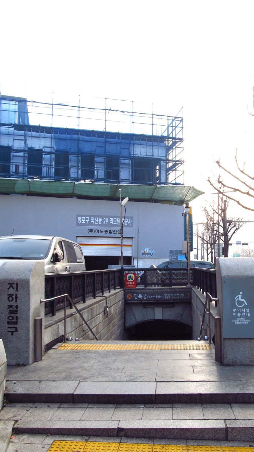 A Gyeongbokgung station entrance, exit 4, with stairs going down, a blue sign reading 경복궁 Gyeongbokgung 4, and a panel with a wheelchair symbol reading 편의시설 이용안내 Disabled Access Information.