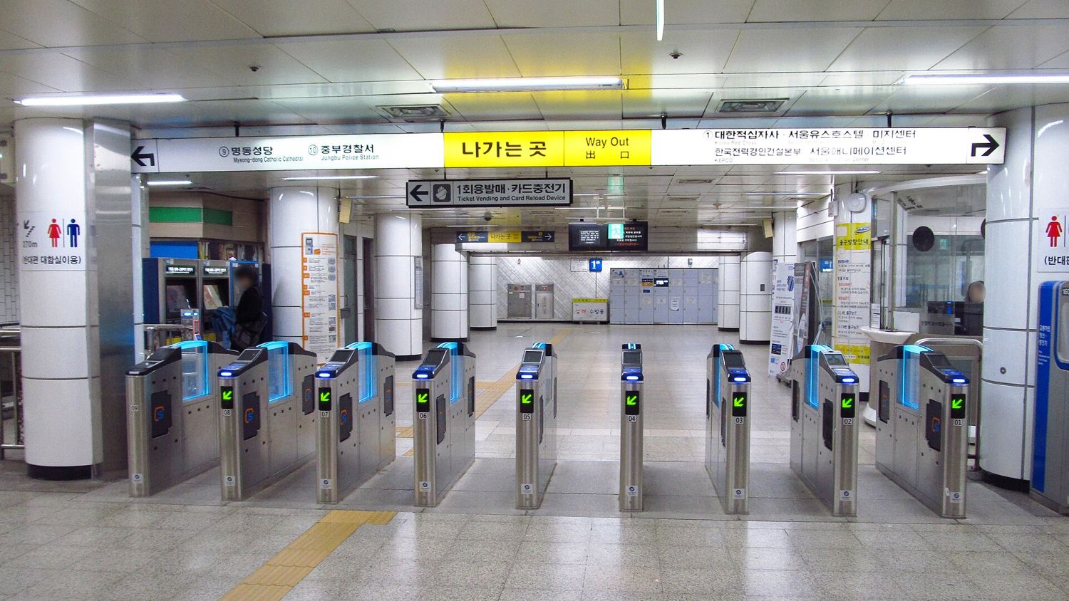The ticket gates at Myeongdong station on Line 4 under a yellow 나가는 곳 Way Out sign, with exit directions to Myeong-dong Catholic Cathedral and the Korean Red Cross.