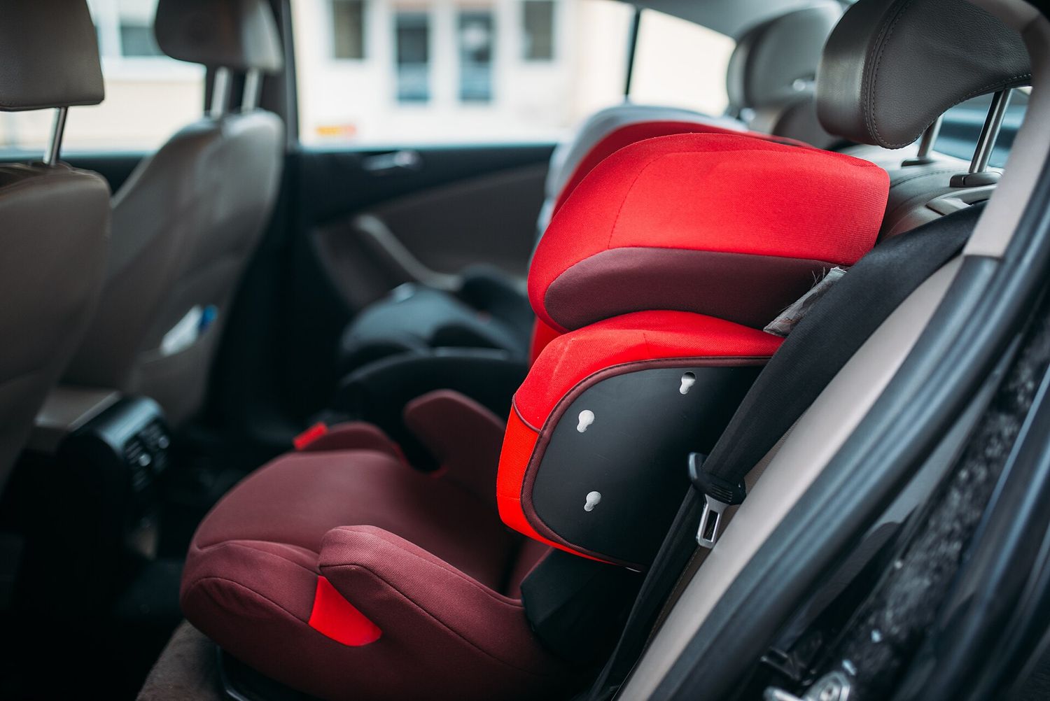 Red and maroon high-back child booster seats fitted on the back seat of a car.