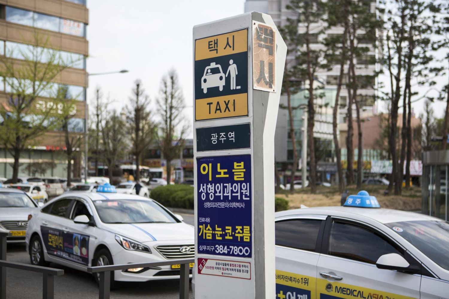 A taxi stand sign reading 택시 TAXI and 광주역 (Gwangju Station) beside a rank of white Hyundai Sonata taxis, April 2018.