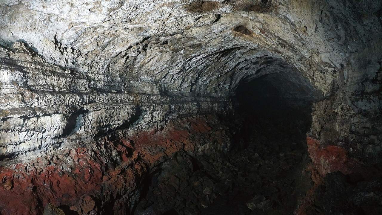A closed lava tube in the Geomunoreum system, its walls banded in white and grey above a reddish floor layer.