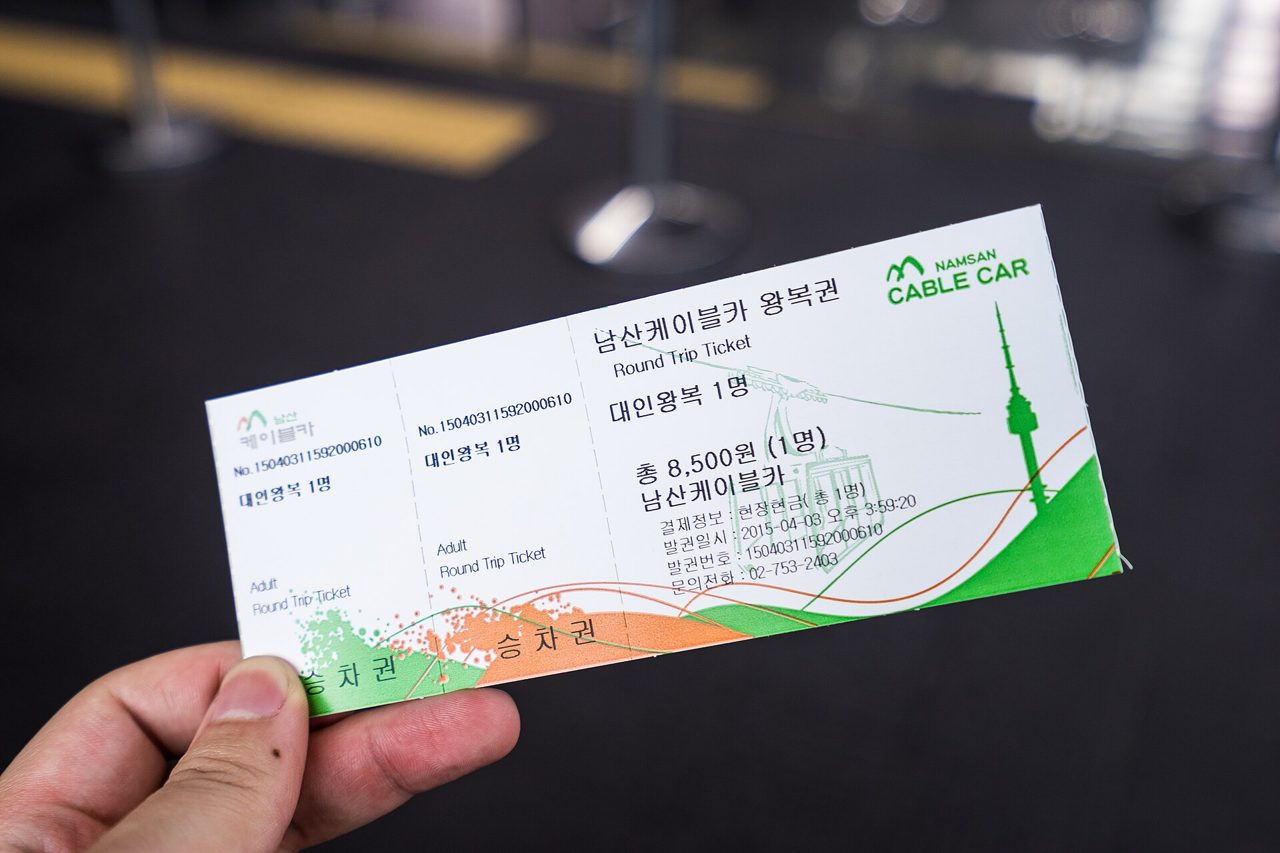 A hand holding a 2015 Namsan Cable Car adult round-trip ticket showing ₩8,500 and "현장현금", paid in cash on site.