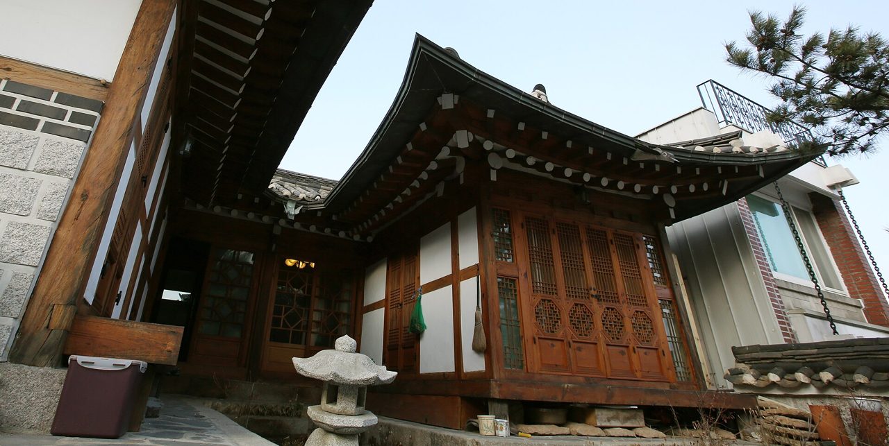 The courtyard of a hanok stay in Bukchon, with tiled eaves, a stone lantern and a modern building behind.