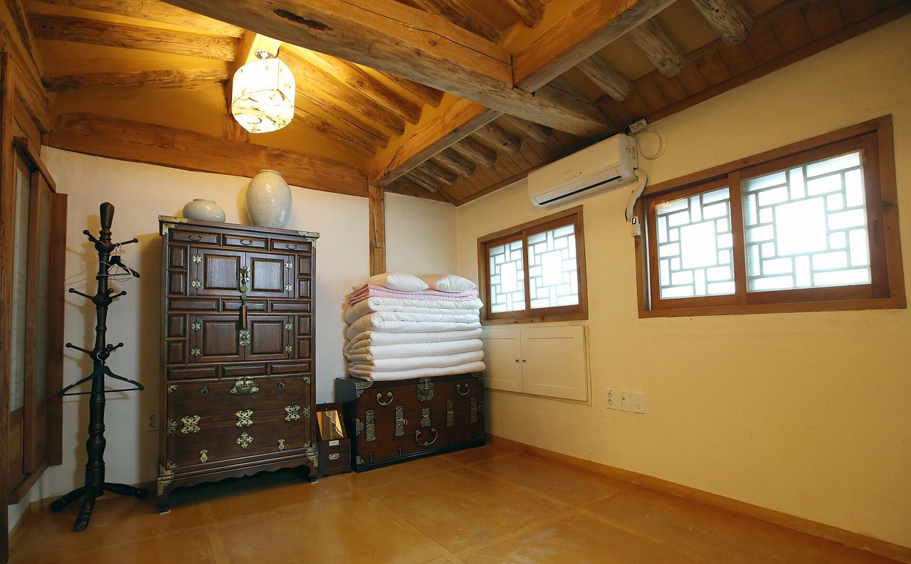 A hanok stay guest room in Bukchon, Seoul, with a yellow floor, folded bedding, lacquered wooden chests and lattice windows.