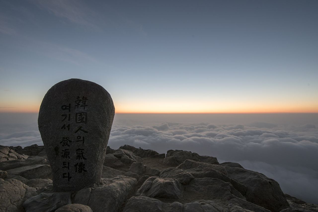 The summit stone of Cheonwangbong on Jirisan at daybreak in November, with a sea of clouds below.