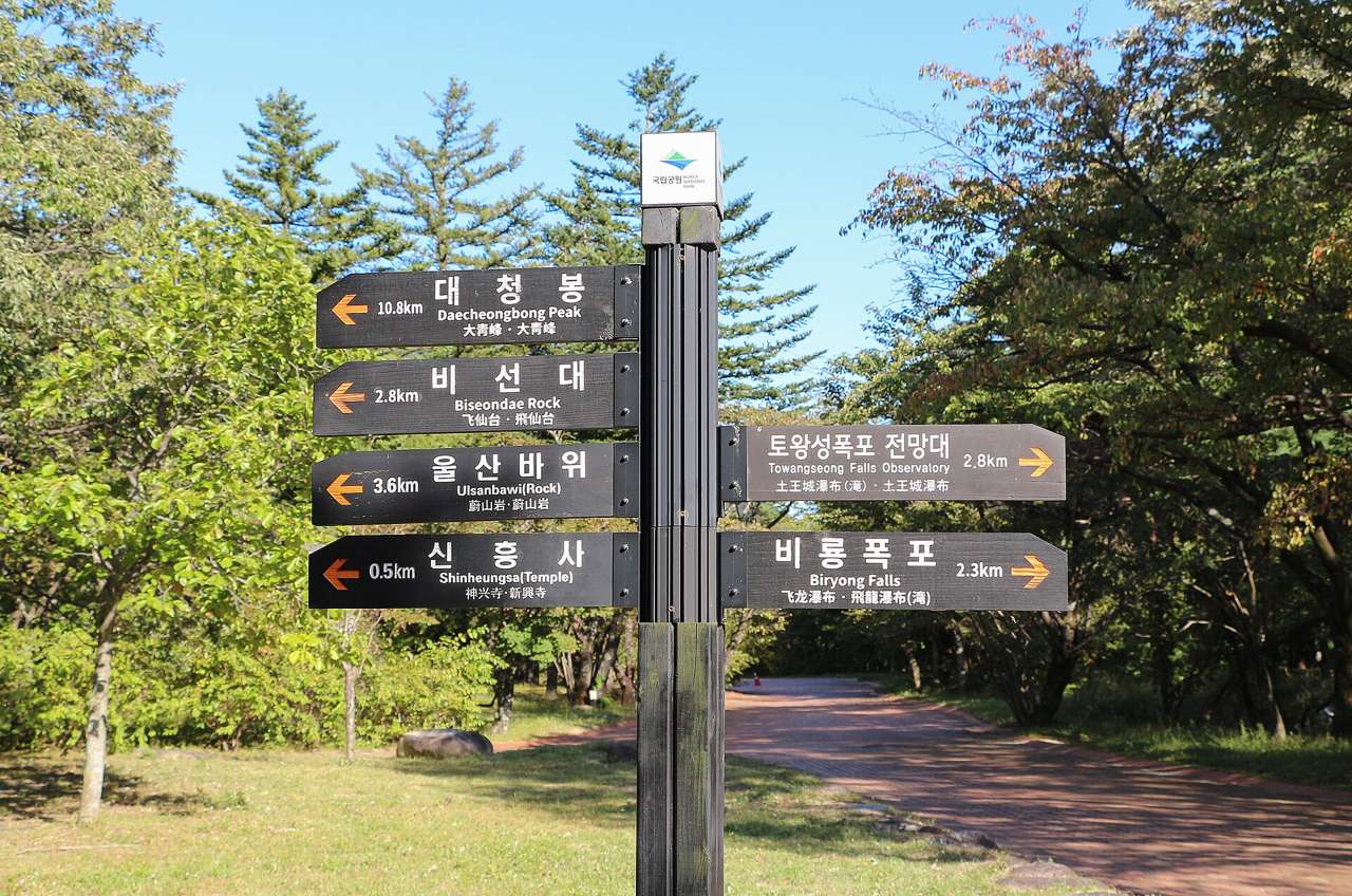A national park signpost at Seoraksan's Sogongwon area with arrows to Daecheongbong 10.8 km, Biseondae 2.8 km, Ulsanbawi 3.6 km, Sinheungsa 0.5 km, Towangseong Falls viewpoint and Biryong Falls, in Korean, English and Chinese.