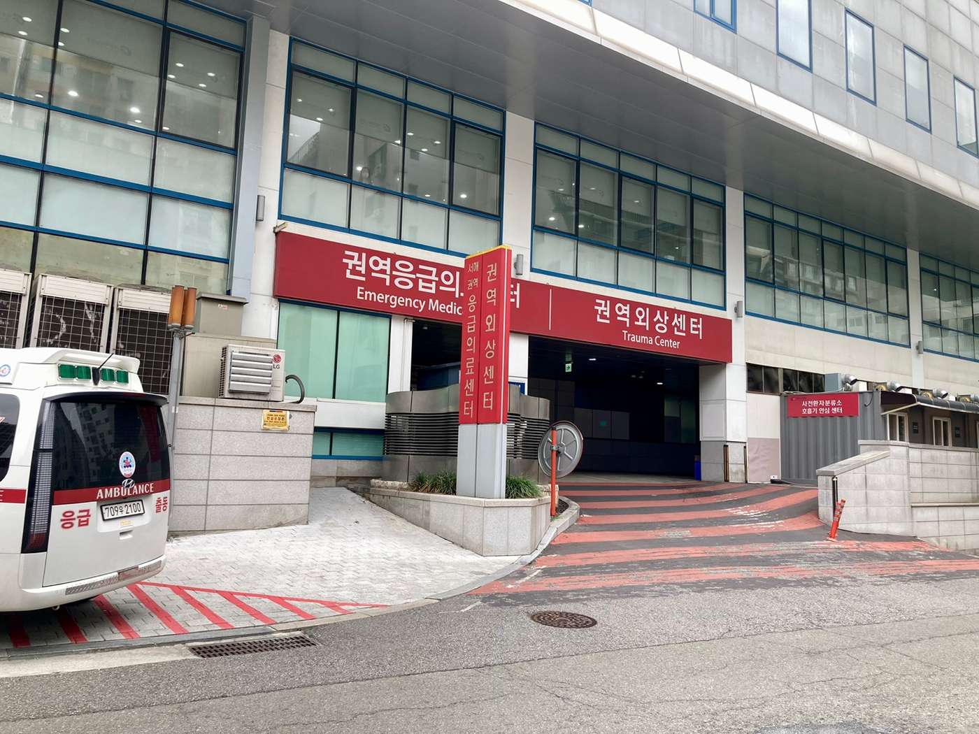 The entrance of Gachon University Gil Hospital's emergency department in Incheon, with large red signs reading 권역응급의료센터 / Emergency Medical Center and 권역외상센터 / Trauma Center, and an ambulance parked at the kerb.