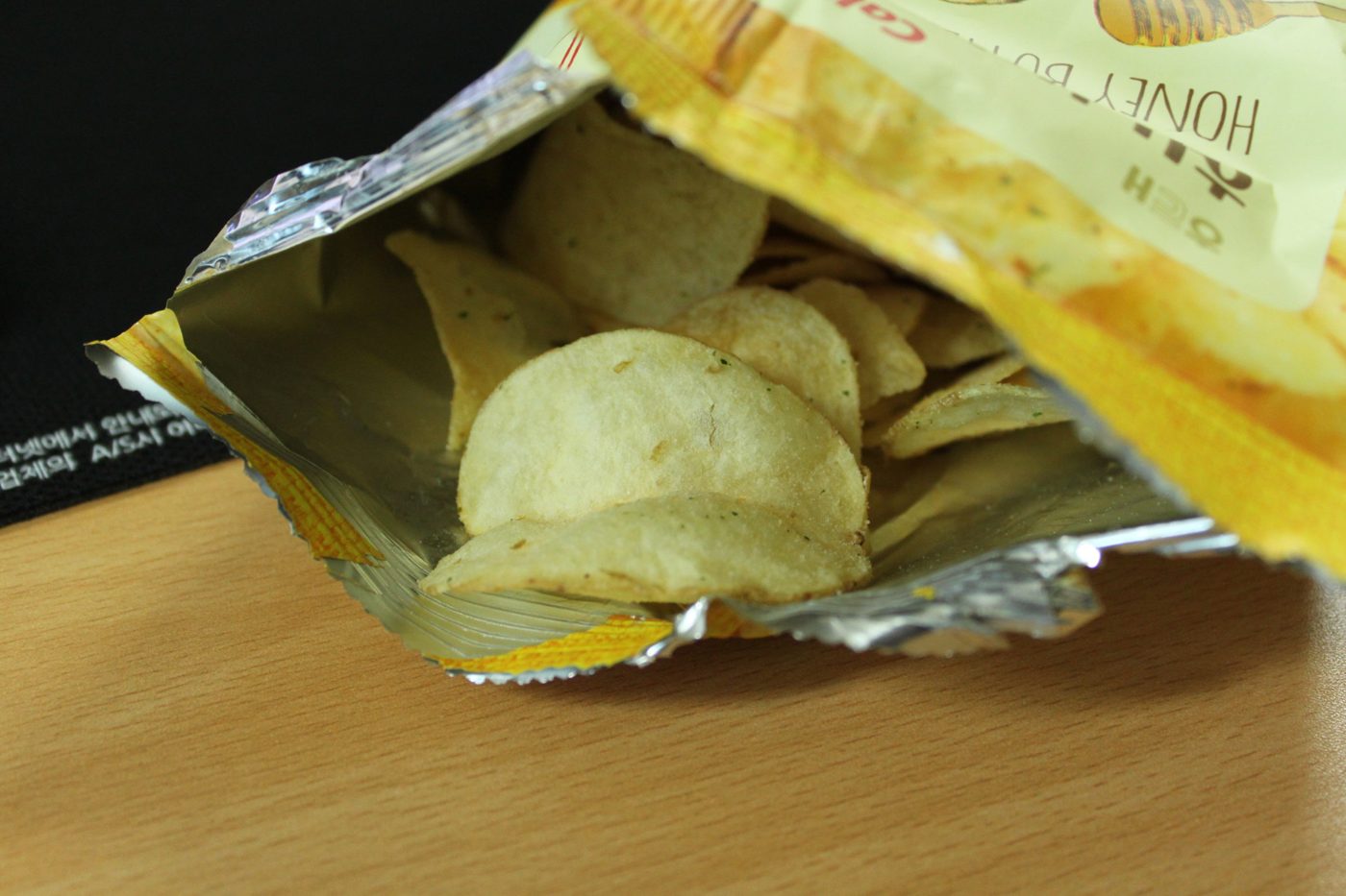 An opened bag of Haitai Honey Butter Chip on a wooden desk, showing the chips and the foil lining of the bag.