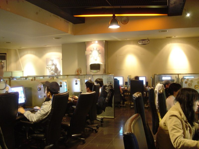 A PC bang in Seoul in 2006: rows of computer stations with high-backed gaming chairs, young people playing under warm ceiling lights.