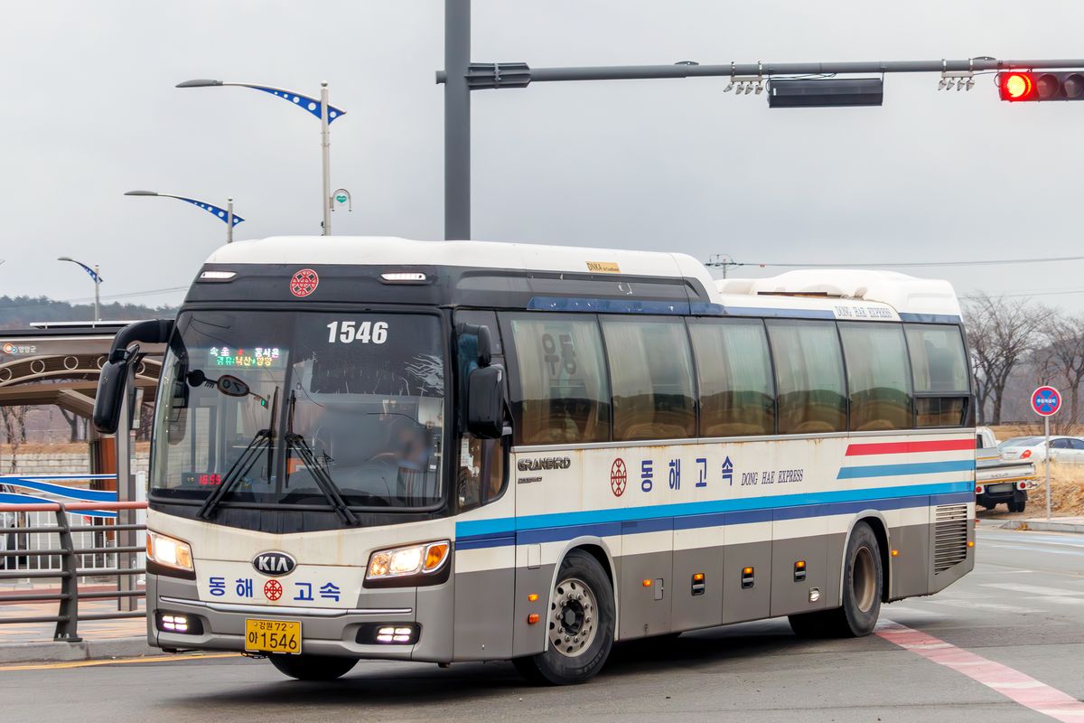 A white Donghae Express (동해고속) deluxe intercity coach, number 1546, with an LED destination board for 속초 to 동서울 via 낙산 and 양양, turning at a road junction in Yangyang under a grey sky.
