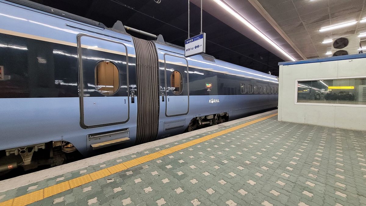 A pale blue KTX-Eum train standing at a covered platform in Cheongnyangni Station, with a hanging sign reading KTX이음 1 2 호차 for car numbers above the yellow safety line.
