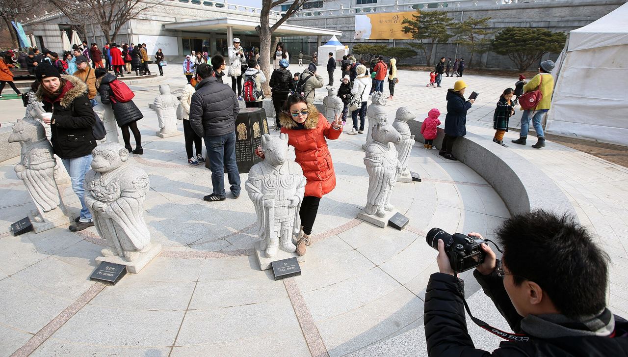 Visitors in winter coats taking photos among the stone statues of the twelve zodiac animals in the courtyard of the National Folk Museum of Korea in Seoul.