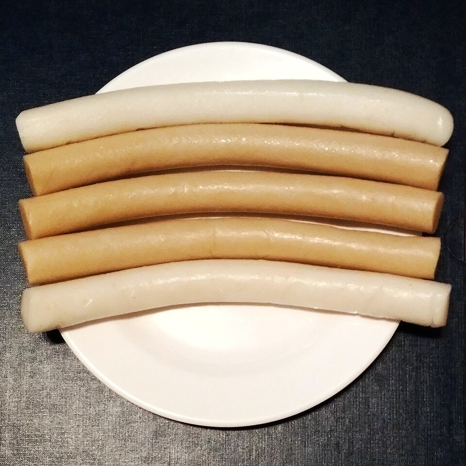 Five long sticks of Korean garaetteok on a white plate: two white rice-cake sticks and three light-brown buckwheat ones, the cylinder rice cakes given on Korea's Garaetteok Day on 11 November.