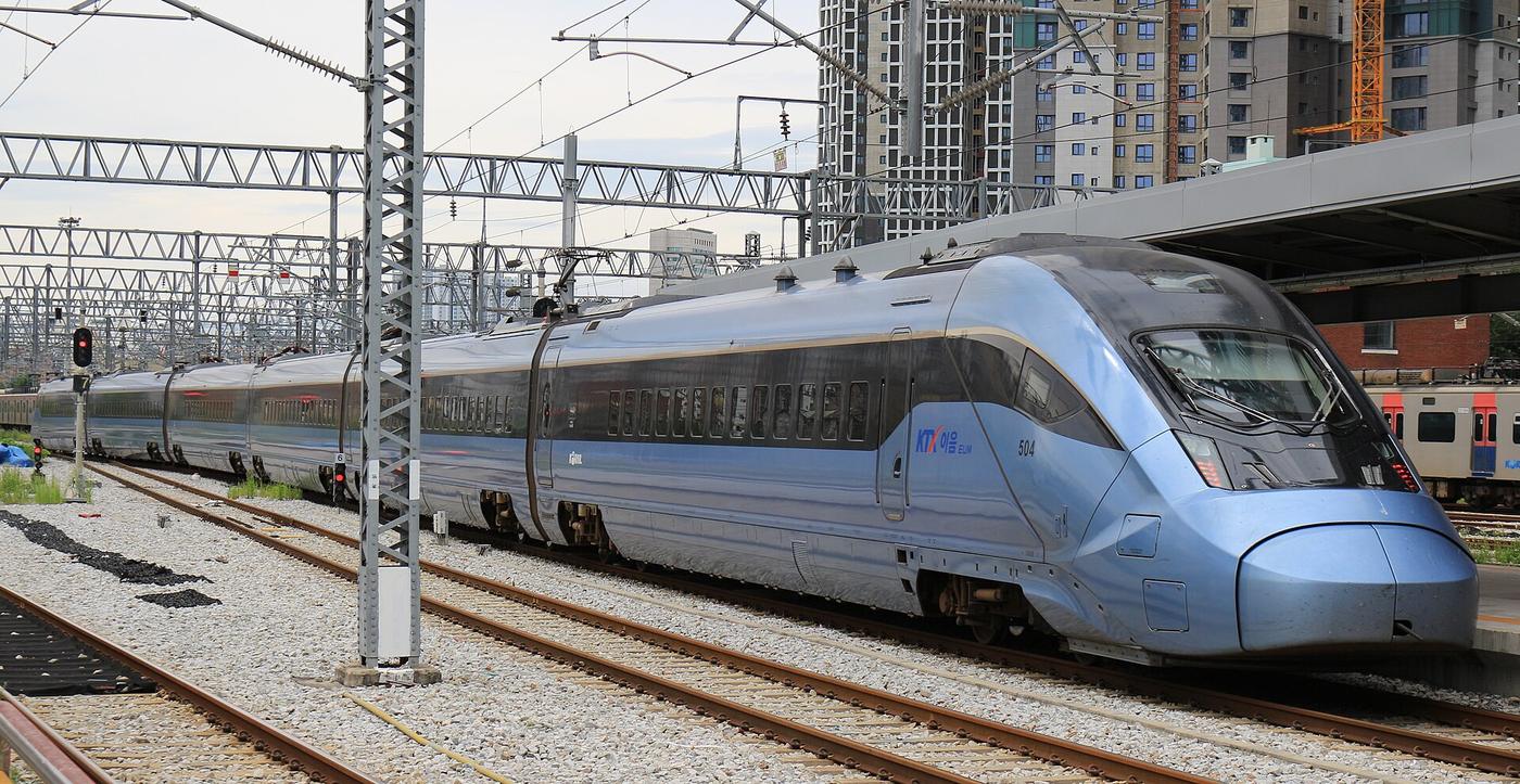 A pale-blue KTX-Eum high-speed train, unit 504, standing at Cheongnyangni Station in Seoul, with the KTX 이음 logo on its side and apartment towers behind the overhead wires.