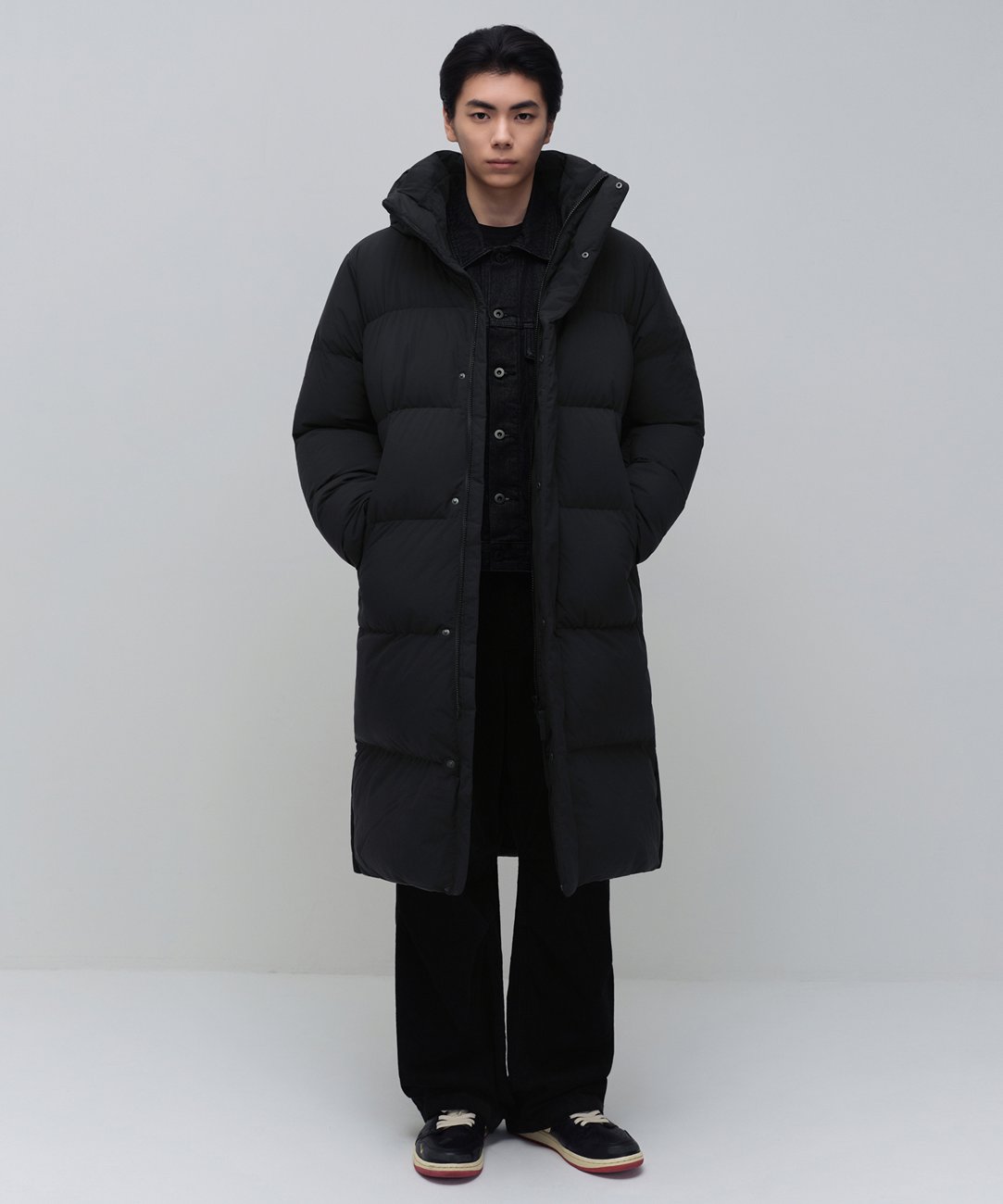 Musinsa Standard's Long Down Bench Parka in black, a hooded below-the-knee quilted parka with snap front, worn open over a denim jacket.