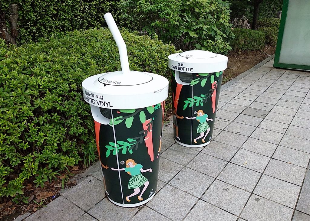 Two street recycling bins in Seocho-gu, Seoul, shaped like giant takeaway cups with straws, labelled 플라스틱·비닐 PLASTIC·VINYL and 캔·병 CAN·BOTTLE.
