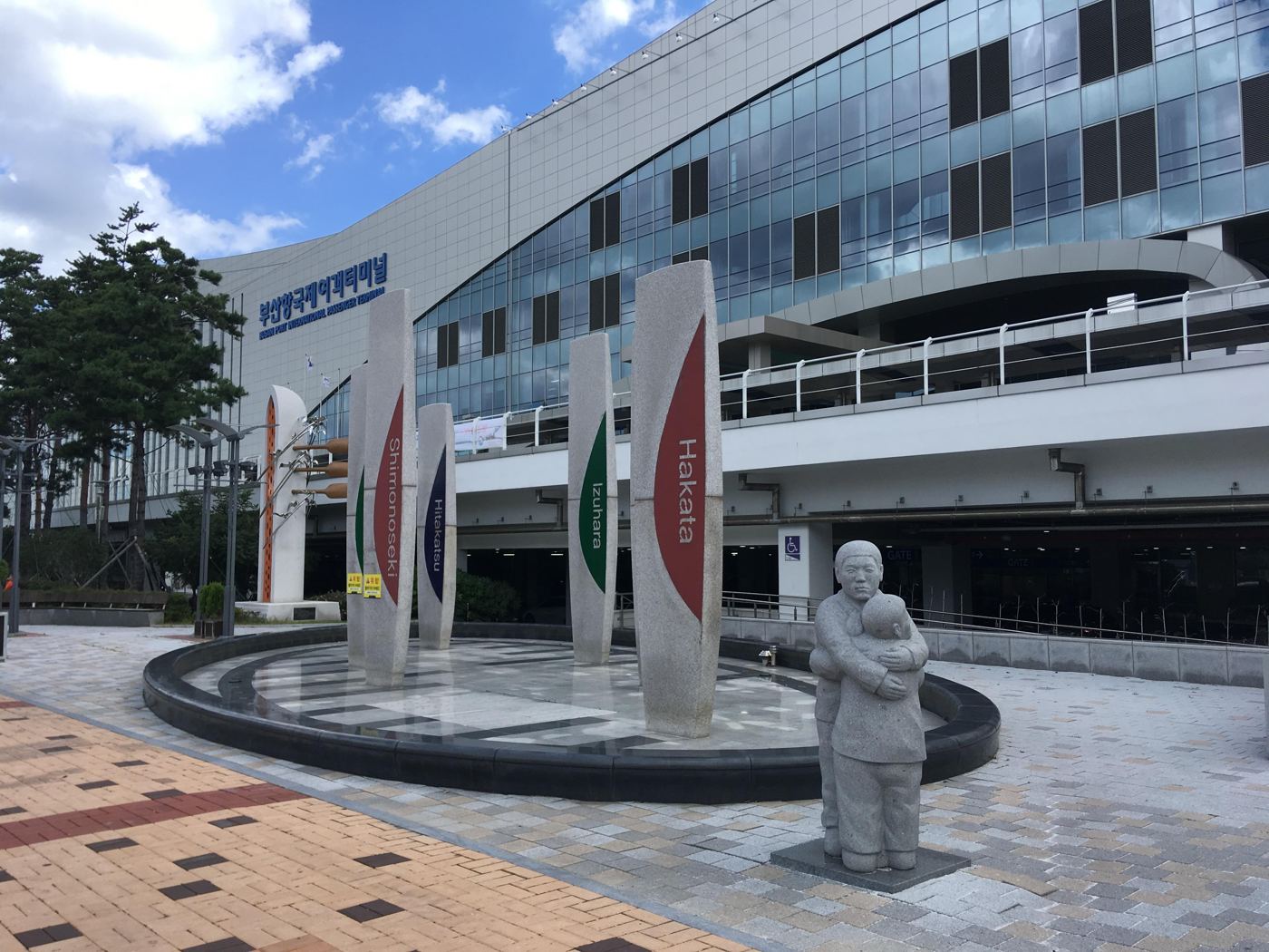 Busan Port International Passenger Terminal, a large glass-fronted building, with stone pillars in front naming the ferry destinations Shimonoseki, Hitakatsu, Izuhara and Hakata.