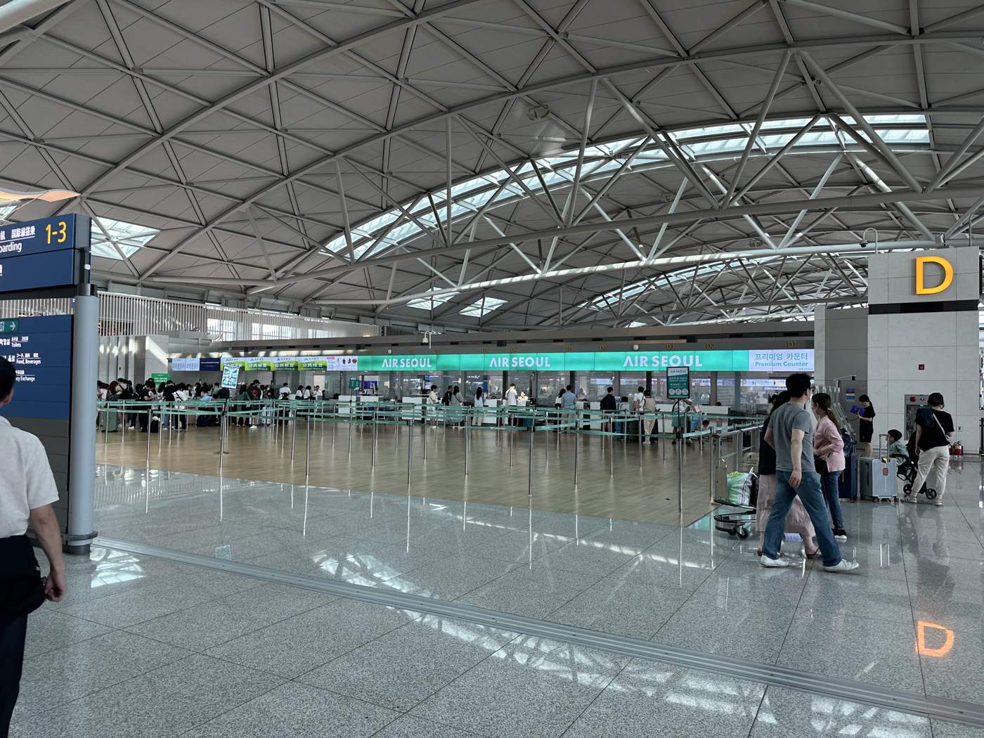 Air Seoul's green check-in counters in an Incheon Airport departures hall, with queues of passengers and a sign for row D.