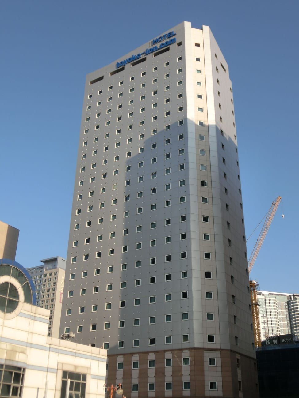The Toyoko Inn Busan Haeundae No.2 tower with the toyoko-inn.com sign on top, against a blue sky.