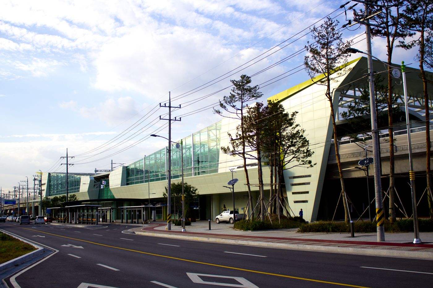 The long, glass-fronted Gonjiam Station building on the Gyeonggang Line, with pine trees and a bus shelter along the road in front.