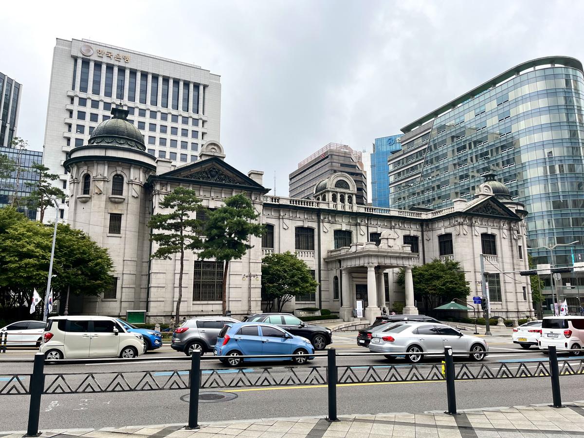 The former Bank of Korea headquarters in Seoul, a pale stone building from 1912 with a domed corner tower, arched windows and a columned porch, now the Bank of Korea Money Museum, with the modern Bank of Korea tower behind it and traffic on the road in front, photographed in September 2023.