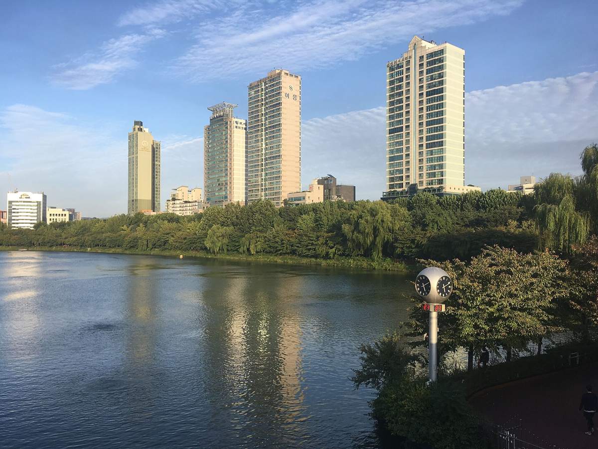 Seokchon Lake in Songpa, Seoul, on a clear autumn afternoon: still water, willow trees along the bank and high-rise apartments behind.