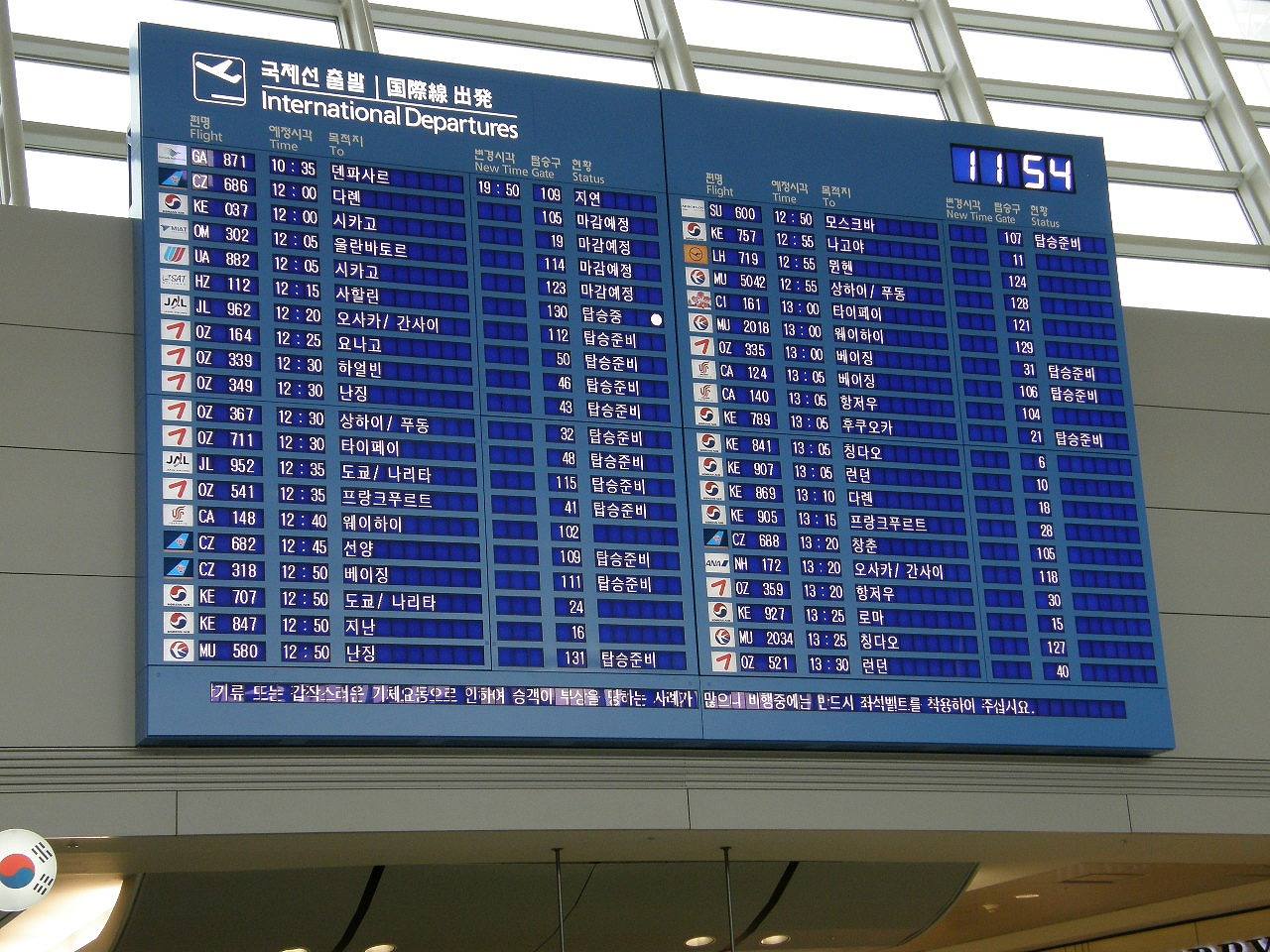 The International Departures board at Incheon International Airport: a large blue display headed 국제선 출발 / International Departures with two columns of flights, airline logos, departure times and Korean destination names; the top line shows a Garuda Indonesia flight to Denpasar scheduled at 10:35 with a new time of 19:50 and the status 지연 (delayed).