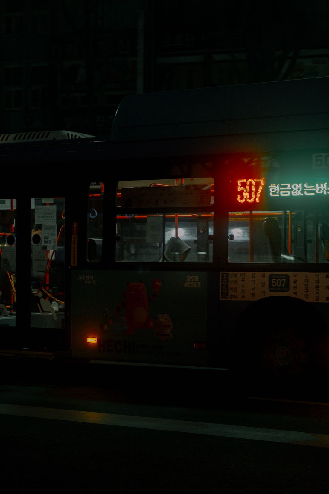 A blue Seoul city bus on route 507 at night, its side display showing the route number and the words 현금없는버스, cashless bus, with a route list printed on the side panel.